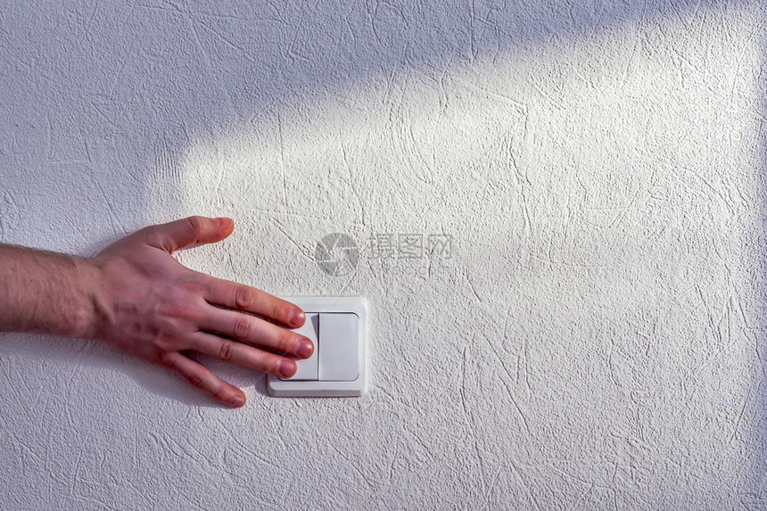 一个人在白石墙上转动电灯开关的手图片