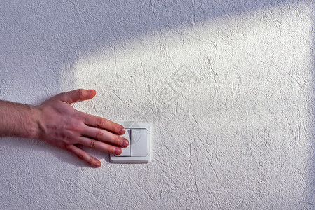 一个人在白石墙上转动电灯开关的手图片