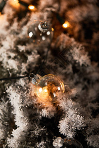 透明的圣诞节球和雪中小枝上的黄色灯光有选择焦点图片