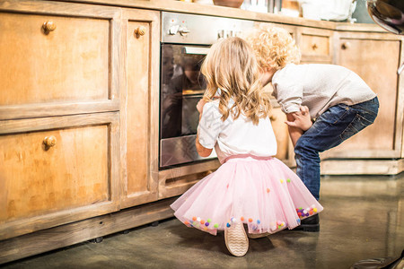 小男孩和小女孩在厨房的烤箱里看图片