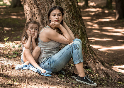 公园树旁一个小女孩和母亲的悲伤情绪家庭关系的概念图片