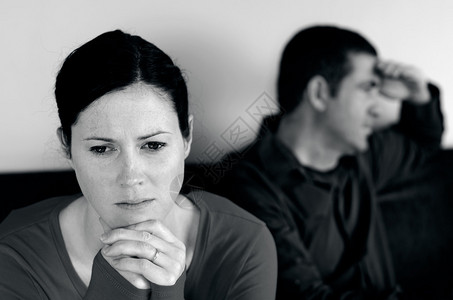坐在沙发上因意见分歧而闹翻的不幸年轻夫妇的画像前面的女人和后面的男图片
