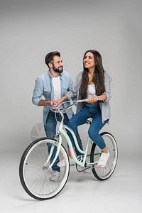 男人帮助快乐的女子骑着单车在灰图片