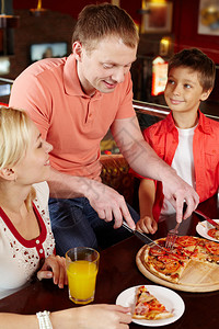 一家人在等他们的父亲切一块开胃的比萨饼图片