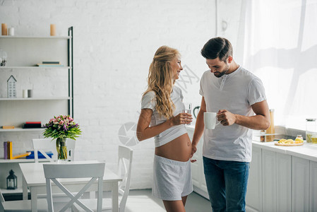 男人拿着一杯咖啡看着家里厨房里怀孕妻图片