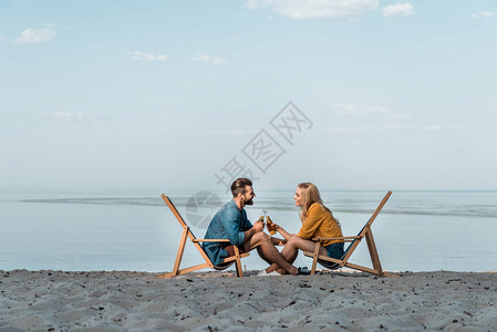 一对夫妇坐在沙滩椅上拿起酒瓶干杯图片