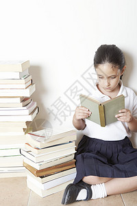 年轻的女学生坐在家里成堆的书旁边看书图片