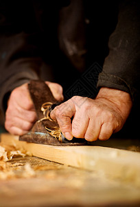 做木工的老人或木匠在他的工作室里用手动平面刨木板的表面图片