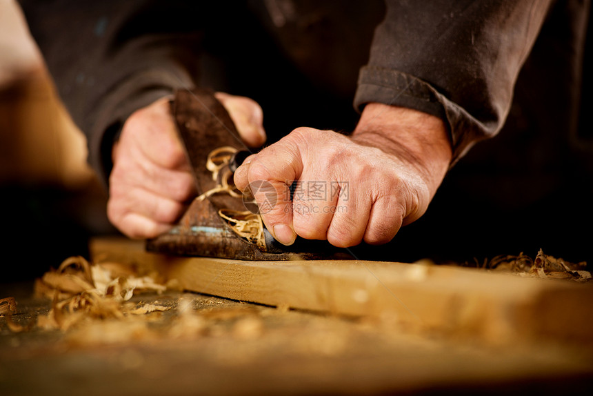 做木工的老人或木匠在他的工作室里用手动平面刨木板的表面图片