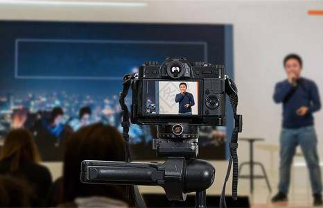 艺术节舞台主带麦克风的专业数码无反相机三脚架录制亚洲演讲者在舞台研讨会上的视频博客摄影师相机或视频和背景