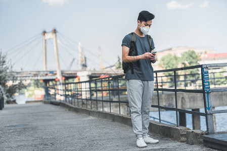 戴防护面具的亚洲青少年使用智能手机图片