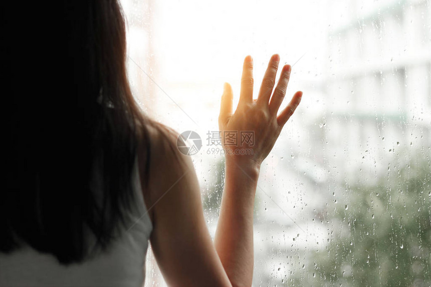悲哀或孤独的女人透过玻璃窗看着城市背景下着图片