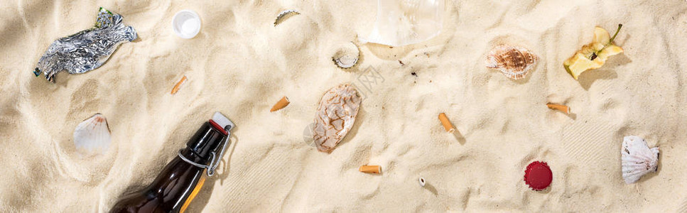 贝壳瓶盖散落的烟屁股苹果芯玻璃瓶和沙上图片