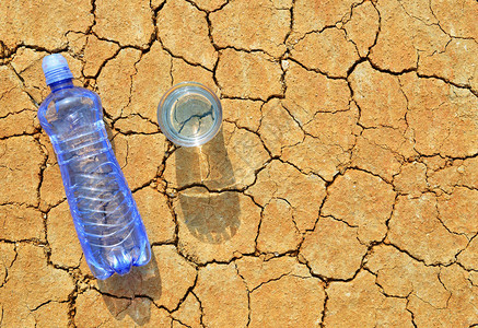 水瓶和水杯在干裂土壤上全图片