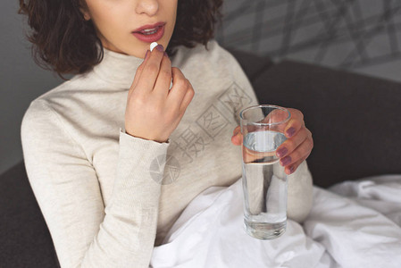 生病妇女在家里服用避孕药和喝杯水的典图片
