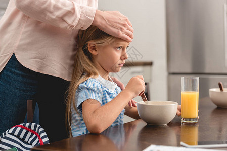 母亲在吃早餐时用手亲检查生病女儿的体温图片