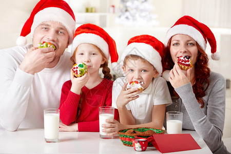 四口的全家在圣诞礼帽上吃果塔和看图片