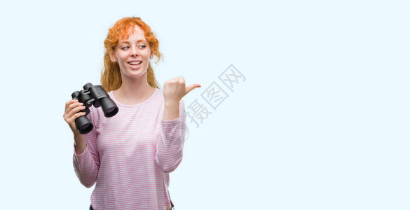 年轻的红发女人透过双筒望远镜指着图片