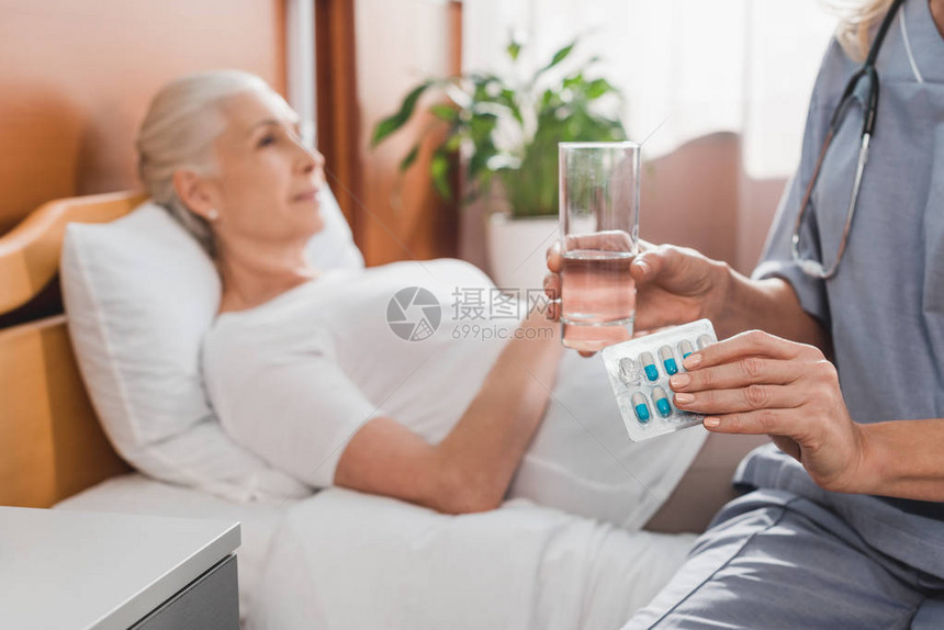 高龄妇女躺在床上时持有避孕药片和水杯图片