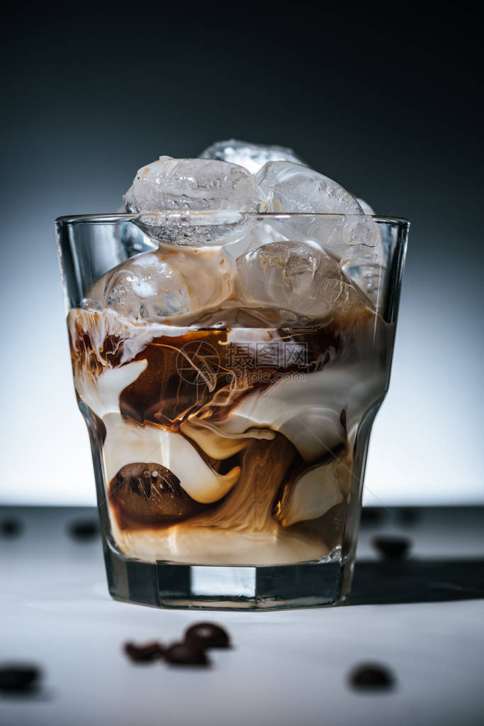 近距离观看冷酿咖啡冰块和深色背景面玻璃桌顶上的烤咖啡豆图片