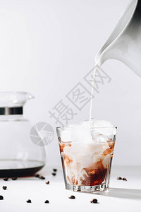将牛奶倒入冷酿咖啡工艺咖啡机和灰底烤咖啡豆的杯中背景图片