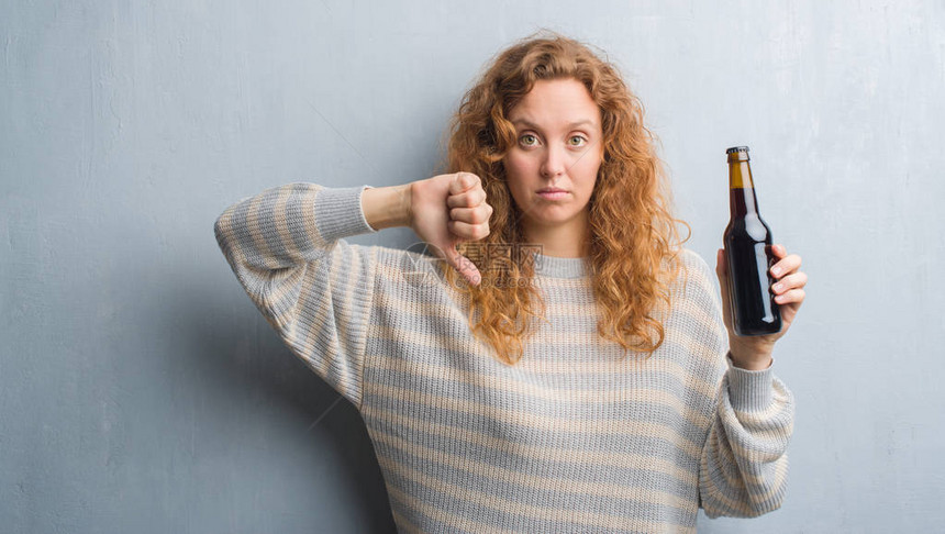 灰熊墙上的红发女青年拿着啤酒瓶满脸愤怒的脸消极的牌子表示不喜欢用拇指向图片