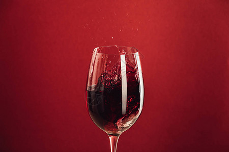 在玻璃杯中喷红葡萄酒在红色上与背景图片