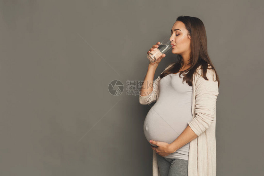 孕妇饮用水年轻的准妈在玻璃灰色工作室背景复印空间中休息怀孕医疗保图片