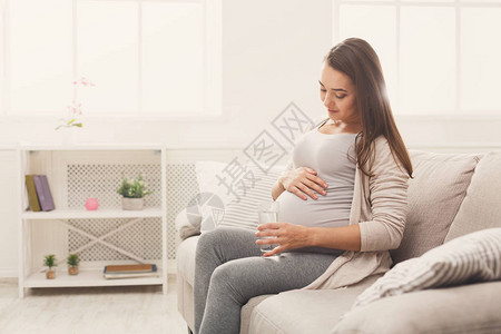 孕妇为她坐在沙发上的肚子提议喝水图片