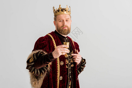 英俊的国王皇冠握着杯子看着在灰色上被图片