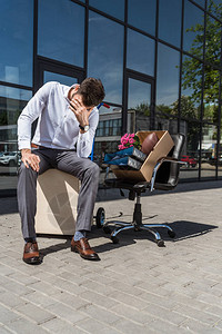年轻情绪低落的经理在被解雇后坐在户外的椅子上坐着图片