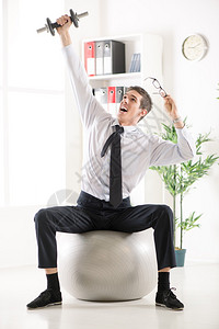 成功的生意人坐在办公室里玩小球和哑铃一起锻炼图片