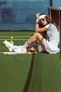 戴太阳镜的时尚女网球运动员在网球场上靠网休息图片