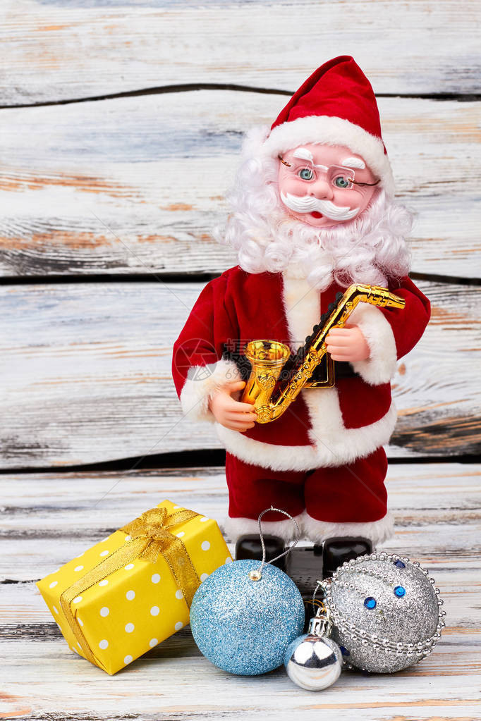 圣诞礼物的圣诞老人玩具可爱的圣诞老人娃站在旧木背景与圣诞玩具和礼物新图片