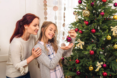 美丽的幸福母亲和女儿在家里一起装饰圣诞树的图片
