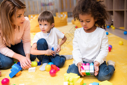 在幼儿园与塑料建筑师一起玩的教育工作者和多族裔儿图片