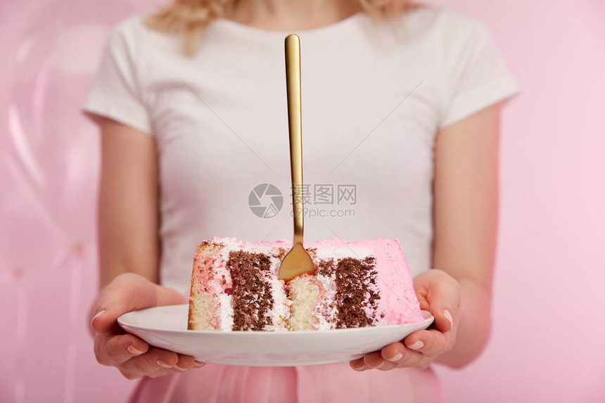 以美味的生日蛋糕和金叉子放在女人手中的板块上有图片