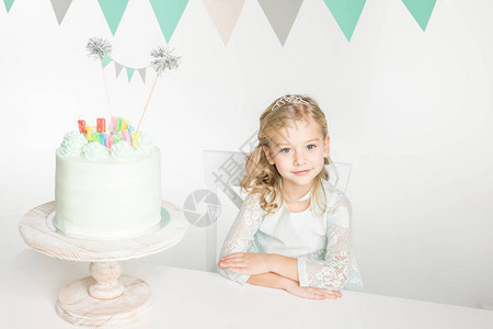可爱的小女孩坐在节庆桌上生日蛋糕在背景图片