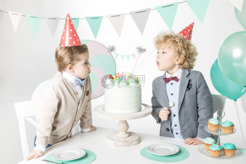 两个小男孩穿着锥帽子在生日蛋糕上吹蜡烛图片