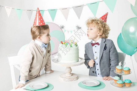 两个小男孩穿着锥帽子在生日蛋糕上吹蜡烛图片
