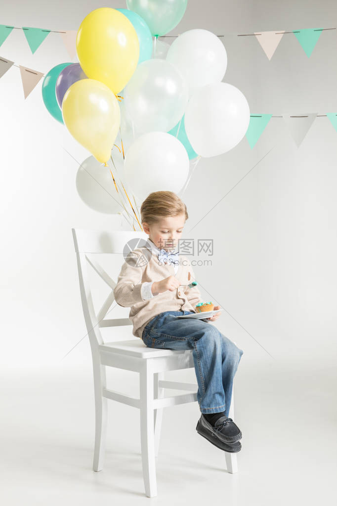 可爱的小男孩坐在椅子上带着气球吃图片