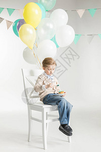 可爱的小男孩坐在椅子上带着气球吃图片