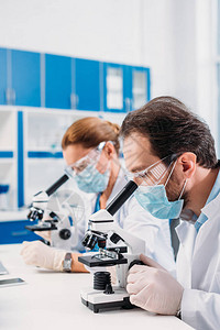 戴医用口罩和护目镜的科学家通过显微镜观察实验室试剂图片