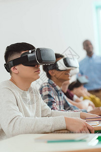 使用虚拟现实头耳和教师站在后面的多族裔中学生的侧高清图片