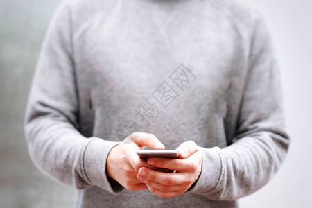 一名青年男子或男孩在用灰色中颜色发短信时手里拿着手机或手图片