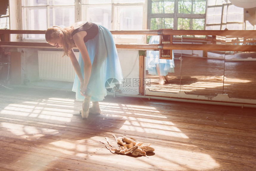 年轻的芭蕾舞女演员或舞者女孩穿上她的芭蕾舞鞋绿松石芭蕾舞裙的女孩旧木地板上的旧芭蕾舞鞋粉色芭蕾尖头木制背景上图片