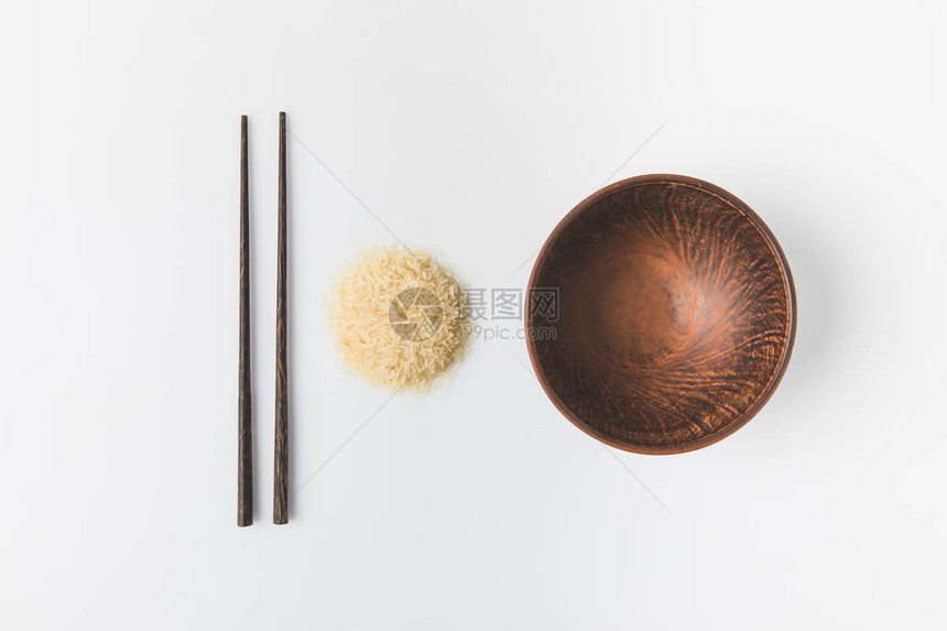 用碗和筷子在白色上隔开的生米堆的顶部视图图片