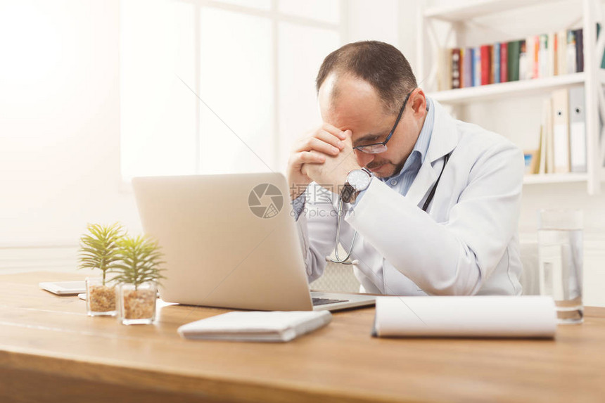 戴着眼镜坐在桌面上的疲惫医生的画像医生在明亮的办公室医学概念图片