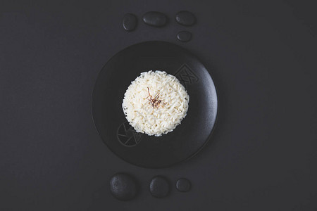 黑桌上有鹅卵石的盘子上美味米饭的顶视图图片