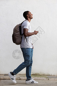 一个微笑的男大学生带袋子和手机走路的全图片